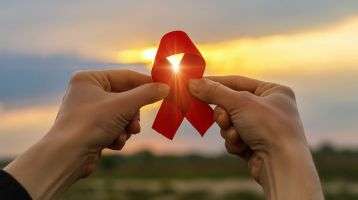 AIDS red ribbon in hands on the background of a sunset.