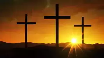 Three crosses on a hill with the setting sun behind them.