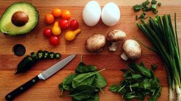 Avacado, onions, tomatos, eggs, mushrooms and leafy greens on a cutting board