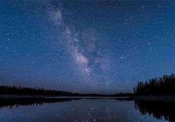 Starry night sky above a tree-lined river