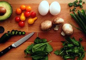 Avacado, onions, tomatos, eggs, mushrooms and leafy greens on a cutting board